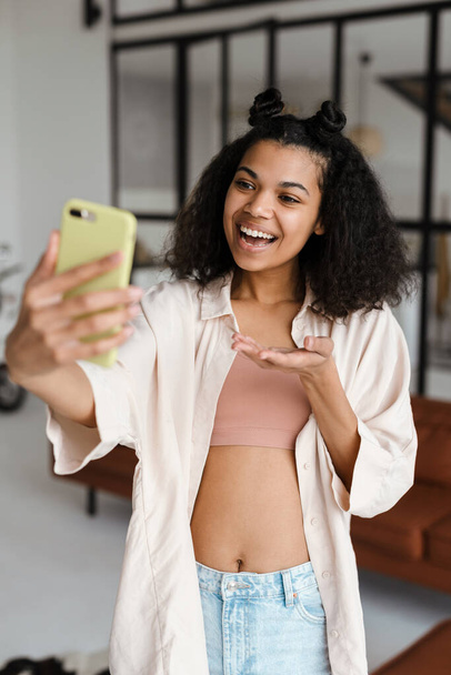 Black young woman holding copyspace while taking selfie on cellphone at home - Photo, Image