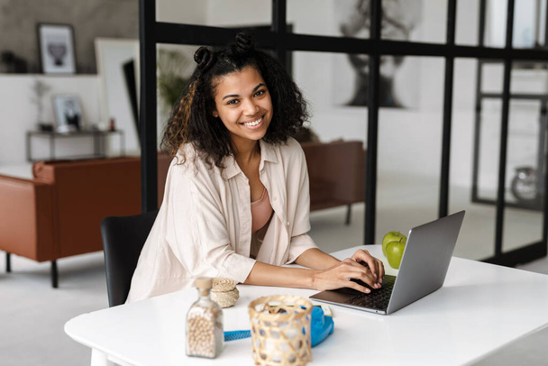 Black young woman smiling and working with laptop at home - Fotoğraf, Görsel