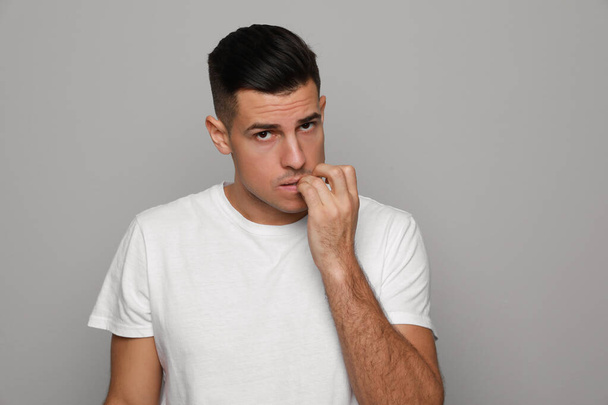 Man biting his nails on grey background. Bad habit - Фото, изображение