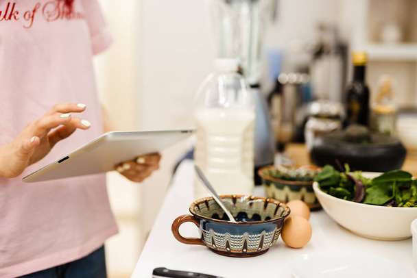 Чернокожая женщина пользуется планшетным компьютером во время приготовления пищи на кухне дома - Фото, изображение