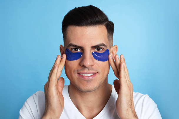Man applying under eye patches on light blue background - Fotografie, Obrázek