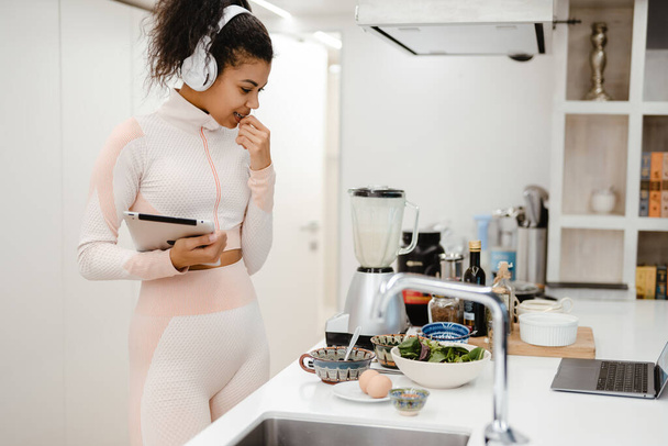 Black woman in headphones using tablet computer while cooking at home - Fotografie, Obrázek