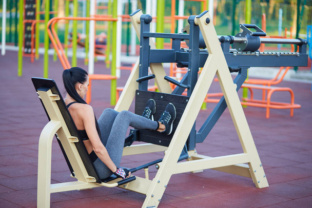 Het sportieve meisje is bezig met fitness buiten op sportsimulatoren. Treinen beenspieren. - Foto, afbeelding