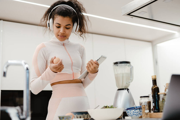 Black woman in headphones using tablet computer while cooking at home - Photo, Image