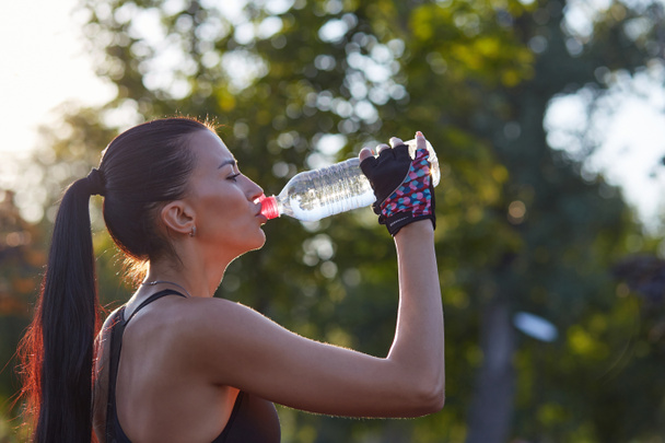Elinde şişe olan kız sporcu parkta egzersiz yaparken su içiyor.. - Fotoğraf, Görsel