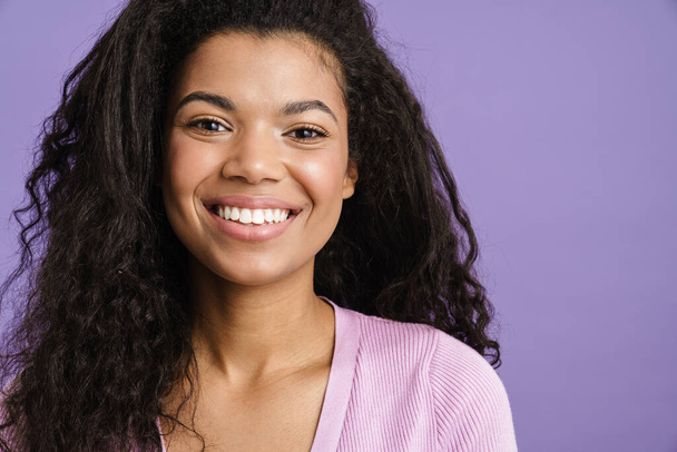 Close up of a happy young african woman in casual clothes standing over violet background, looking at camera, smiling - Φωτογραφία, εικόνα