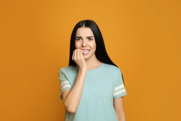Young woman biting her nails on yellow background - Fotó, kép