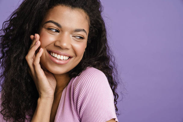 Young black woman with curly hair laughing and looking aside isolated over purple background - Foto, immagini