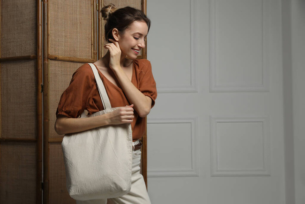 Happy young woman with blank eco friendly bag indoors. Space for text - Φωτογραφία, εικόνα