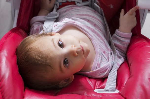 Bebê sentado em cadeira de bebê vermelho e olhando para cima
 - Foto, Imagem