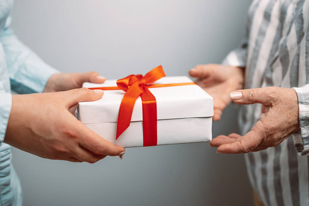 Closeup of two female hands holding red gift box with golden bow against grey background - Foto, immagini