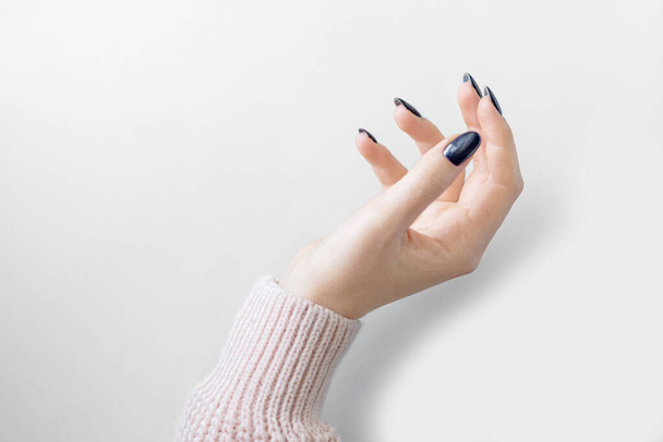 goed verzorgde vrouwelijke hand met een blauwe manicure en een roze trui op een witte achtergrond. isoleren. plaats voor tekst - Foto, afbeelding