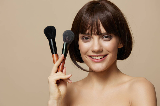 young woman makeup brushes near the face bare shoulders cropped view - Photo, Image