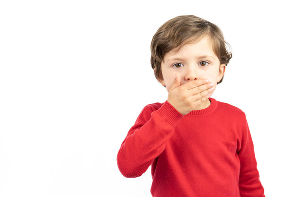 Portrait of a boy in a red sweater with his hands over his mouth. Shocked frightened boy - Foto, Imagen