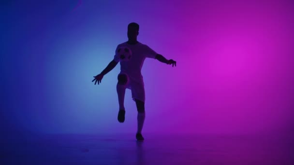 Hombre negro un jugador hace malabares pelota de fútbol en un estudio oscuro con luces de neón en el suelo y rojo y azul efectos de iluminación en cámara lenta. Africano jugador de fútbol profesional - Metraje, vídeo