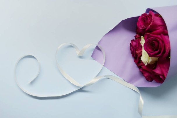 Букет красных роз в фиолетовой упаковке лежит на синем фоне. Сердце из белой ленты - Фото, изображение