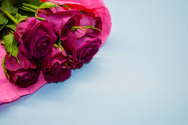 Μπουκέτο με κόκκινα τριαντάφυλλα βρίσκεται σε ένα μπλε φόντο. - Φωτογραφία, εικόνα