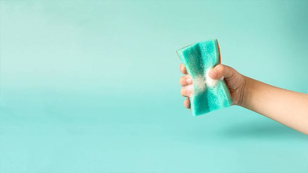 Banner action hand holding a blue sponge with white foam on a blue background. The concept of washing dishes and cleaning - Фото, зображення
