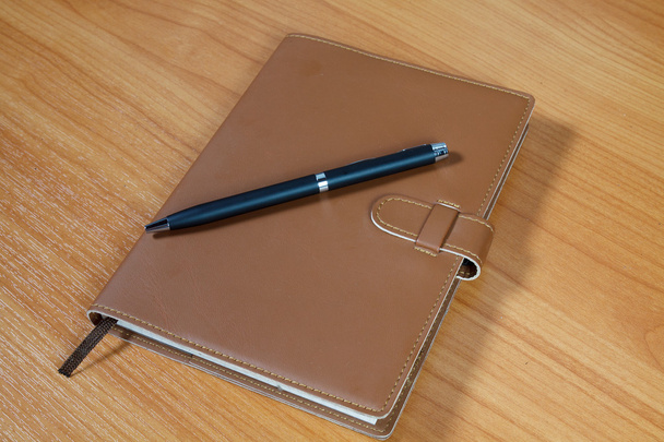 brown notebook and pen over wooden background - Foto, afbeelding