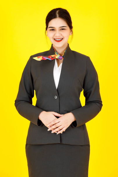 Portret studio schot van Aziatische professionele succesvolle slimme zelfverzekerde vrouwelijke stewardess lucht gastvrouw in formele uniform pak met sjaal staande glimlachende blik op camera poseren op gele achtergrond. - Foto, afbeelding