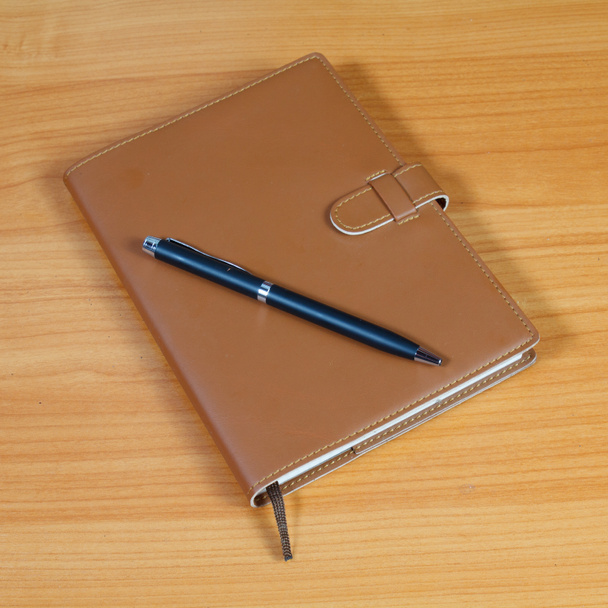 caderno marrom e caneta sobre fundo de madeira
 - Foto, Imagem