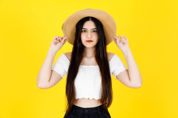 Portrait studio shot of Asian young beautiful sexy long black hair female model wearing crop top outfit dental care braces standing smiling holding hand touching adjusting hat on yellow background. - Foto, Imagem
