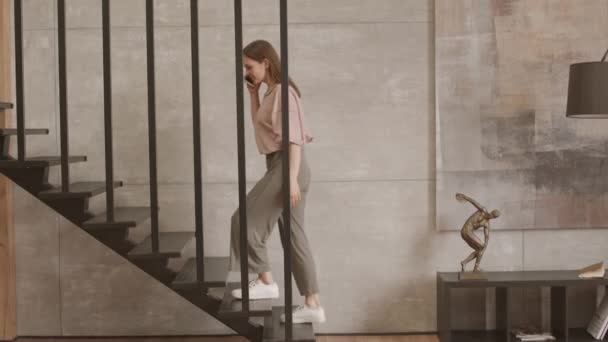 Slowmo πλάνο της νεαρής καυκάσιας ανεξάρτητης γυναίκας που ανεβαίνει τις σκάλες στο μοντέρνο διαμέρισμα της διπλής όψης έχοντας τηλεφωνική συνομιλία - Πλάνα, βίντεο