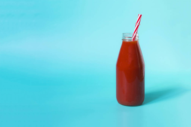 Tomato juice in a transparent bottle with a red plastic tube on a blue background - a place for text - Фото, зображення