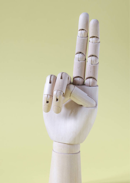 Wooden hand with two fingers raised up on a yellow background vertical orientation. - 写真・画像