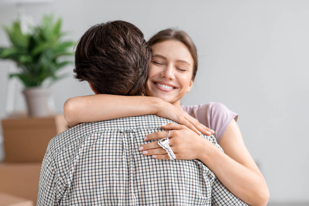 Smiling happy pretty young european wife hugs husband and shows key from new own apartment in room interior - Фото, зображення