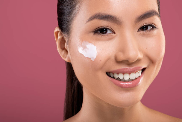 Smiling asian woman with moisturizer cream on her cheeks - Photo, Image