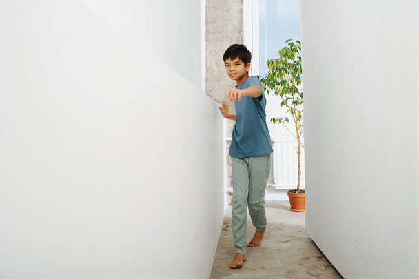 Handsome indian boy walking in a corridor between a wall and a set. Looking at the camera. Inside an apartment. - Fotografie, Obrázek