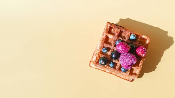 Soft waffle with a decor of black and red berries on a yellow background natural hard light. - Foto, afbeelding