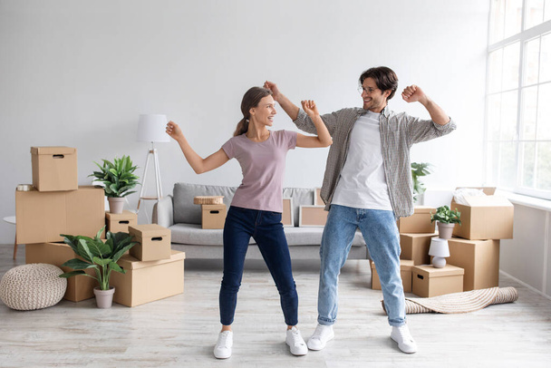 Satisfied excited european young man in glasses and woman dancing in living room interior - Fotó, kép