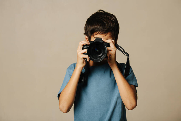 Indian boy taking a photo with a digital camera over beige background. Holding device over his face. - Foto, Imagen