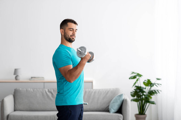 Concentrated serious millennial european guy doing strength exercises for arms and lifting dumbbells - Photo, Image