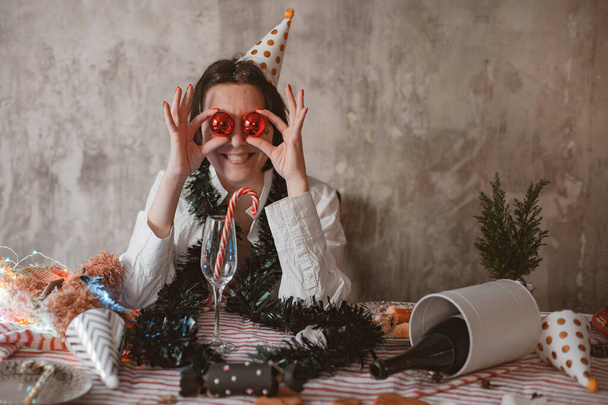 Joven mujer alegre en fiesta festiva sombrero cómicamente cubriendo sus ojos con burbujas brillantes de Navidad - Foto, imagen