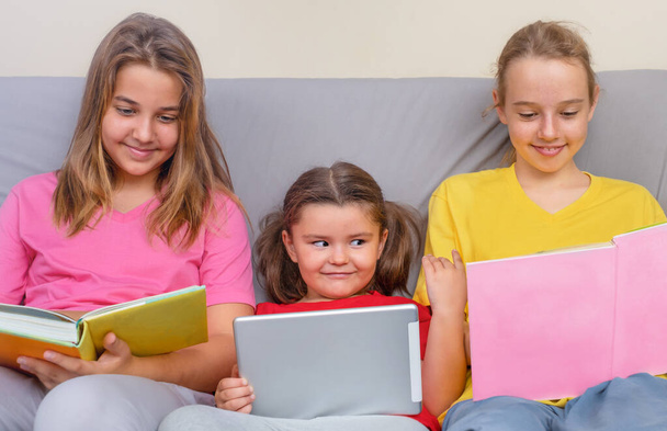 Une enfant fille avec une tablette regarde dans les livres d'un adolescent sur le canapé - Photo, image