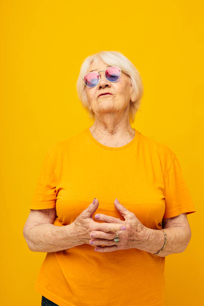 Portrait of an old friendly woman in a yellow t-shirt posing isolated background - Φωτογραφία, εικόνα