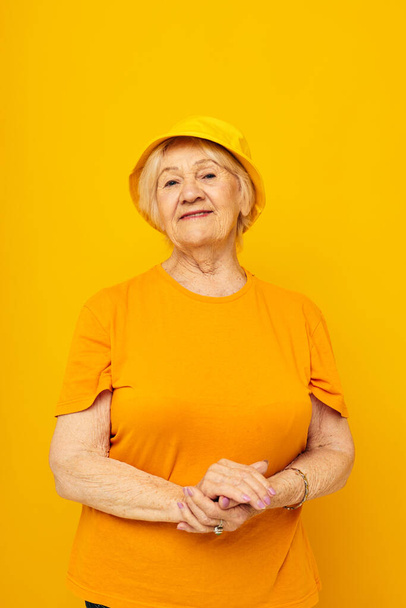 smiling elderly woman in casual t-shirt yellow panama yellow background - 写真・画像