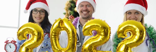 Joukkue lääkäreitä punaisissa korkeissa pitää numeron 2022 taustaa vasten uudenvuoden puu - Valokuva, kuva