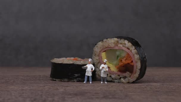 Schinken-Gemüse-Gimbap mit braunem Reis und zwei Miniaturköchen. Miniaturmenschen und Gimbap mit Geschäftskonzept. - Filmmaterial, Video