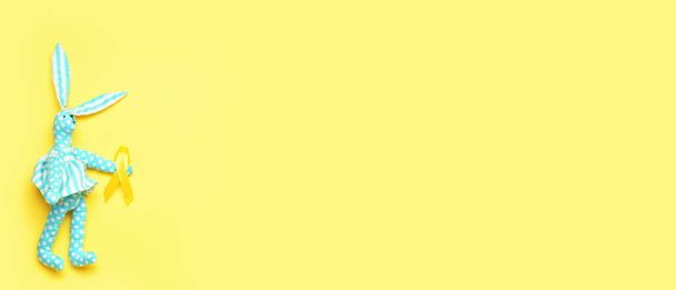 Zabawka Bunny ze złotą wstążką świadomości na żółtym tle z miejscem na tekst. Międzynarodowy Dzień Raka Dzieciństwa - Zdjęcie, obraz