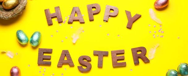Text HAPPY EASTER with chocolate eggs on yellow background - Фото, зображення