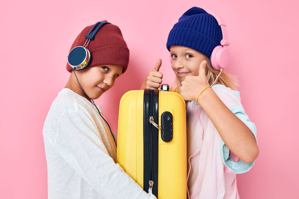 joyful boy and girl stylish clothes suitcase headphones pink color background - Photo, Image