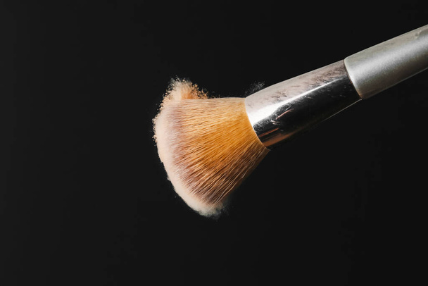 Makeup brush shaking off powder on black background - Foto, Imagem