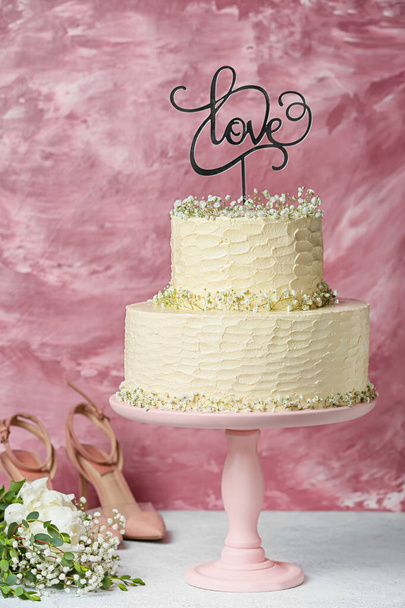 Dessert stand with beautiful wedding cake and topper with word LOVE on table - Фото, зображення