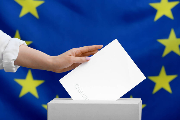 Mujer votante con papel cerca de urnas contra bandera de la Unión Europea - Foto, Imagen