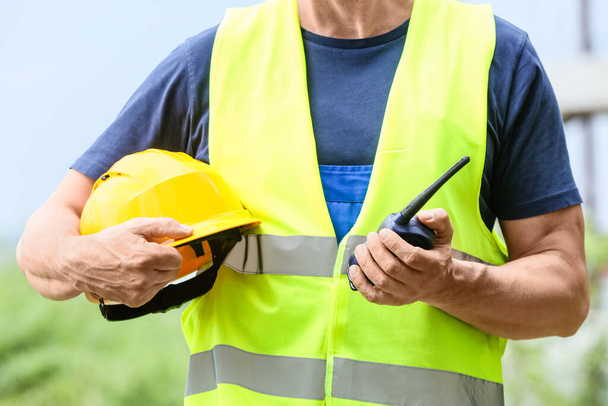 Mannelijke werknemer met veiligheidshelm en radiozender op bouwplaats - Foto, afbeelding