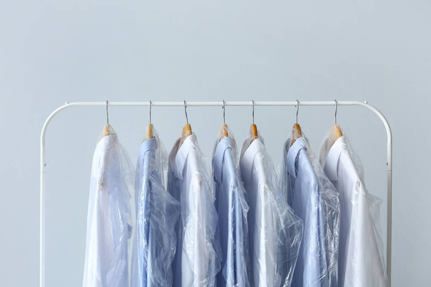 Rack met schone shirts in plastic zakken op grijze achtergrond - Foto, afbeelding